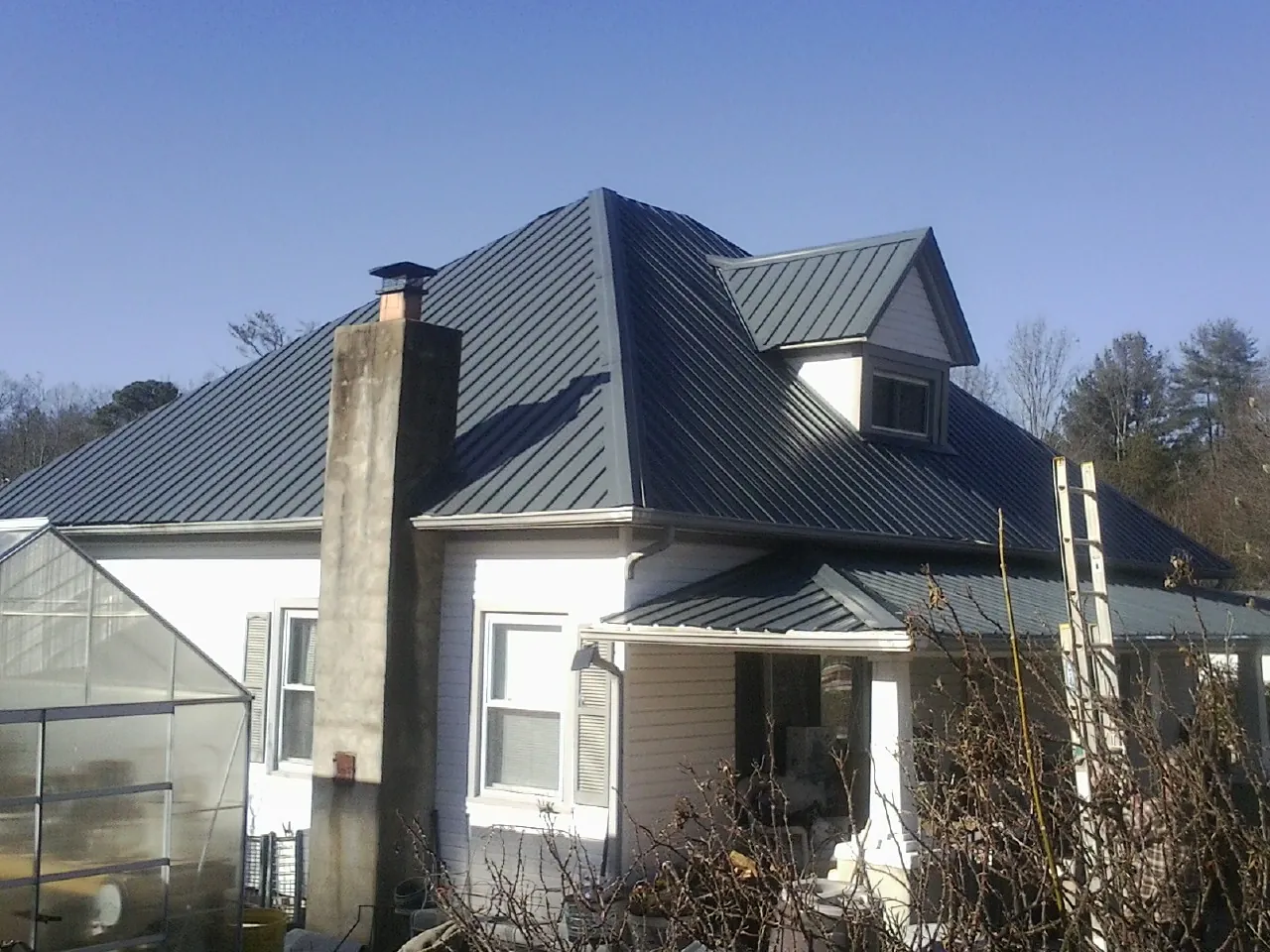Dark blue standing seam metal roof on a white farmhouse with dormer — Slate & Tile Roof Repair by Roofing Brothers in Fresno