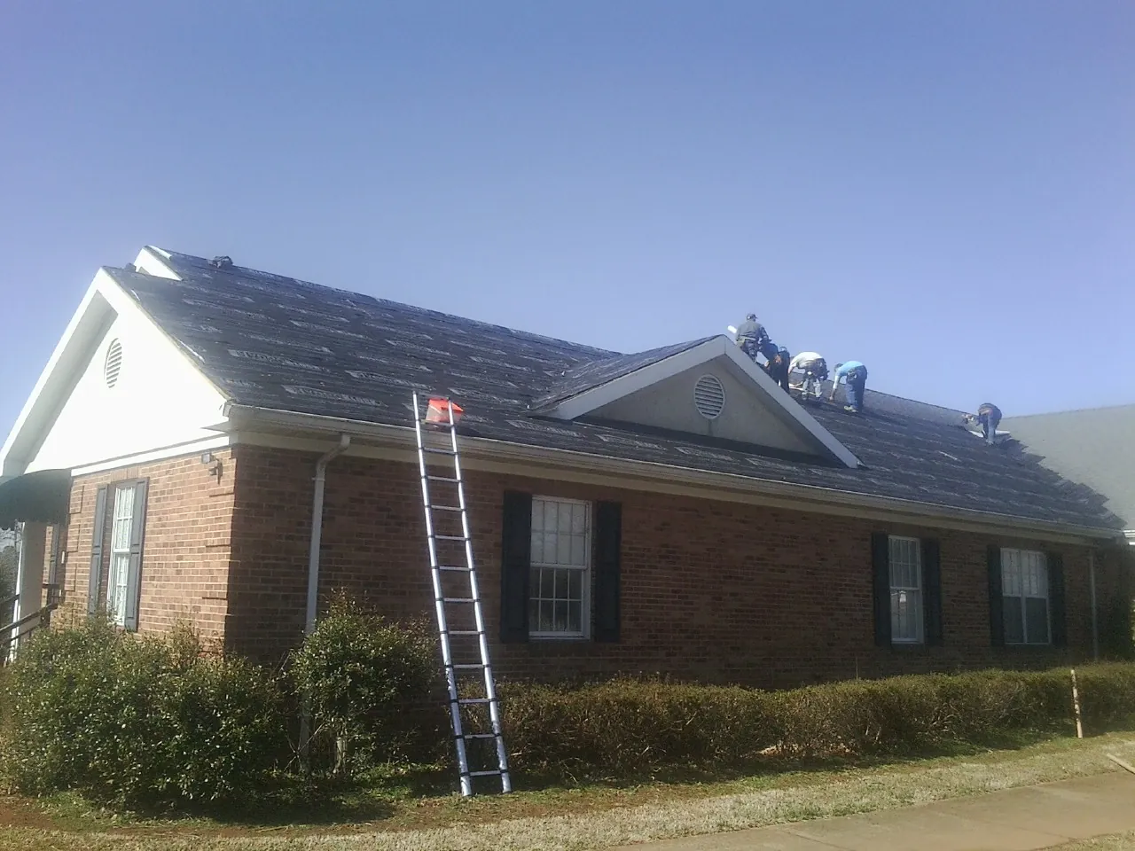 Crew tearing shingles off a brick ranch roof with a ladder set — Emergency Roof Repair work by our crew in Fresno