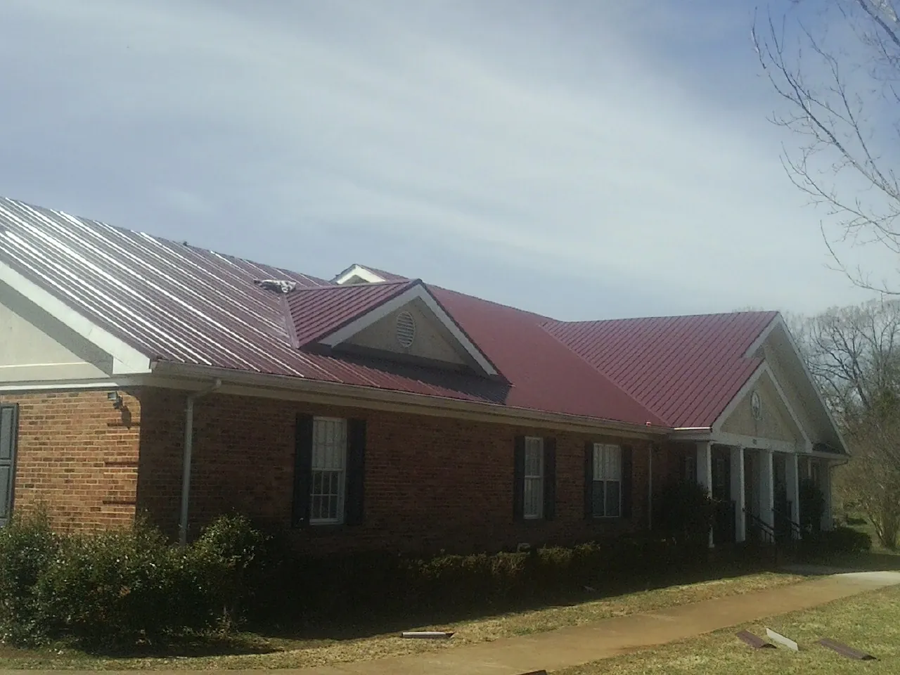 Red metal roof with gabled entries on a long brick building, from a Hail Damage Roof Repair job in Fresno