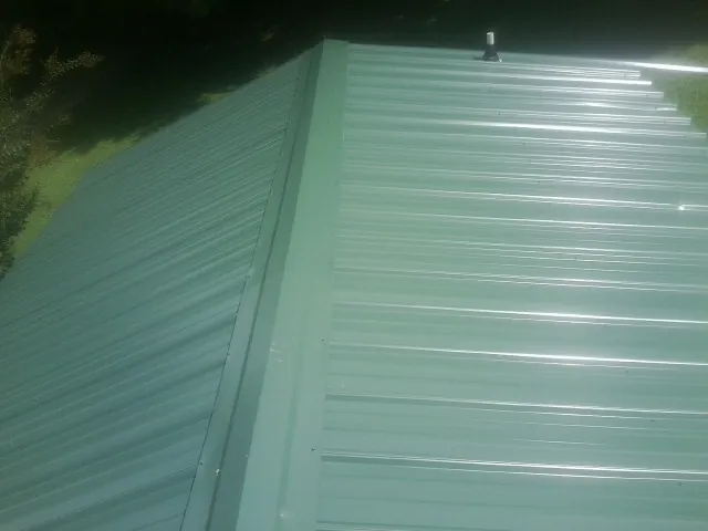 New green metal panels meeting at the ridge of a roof — Flat Roof Repair work by our crew in Fresno