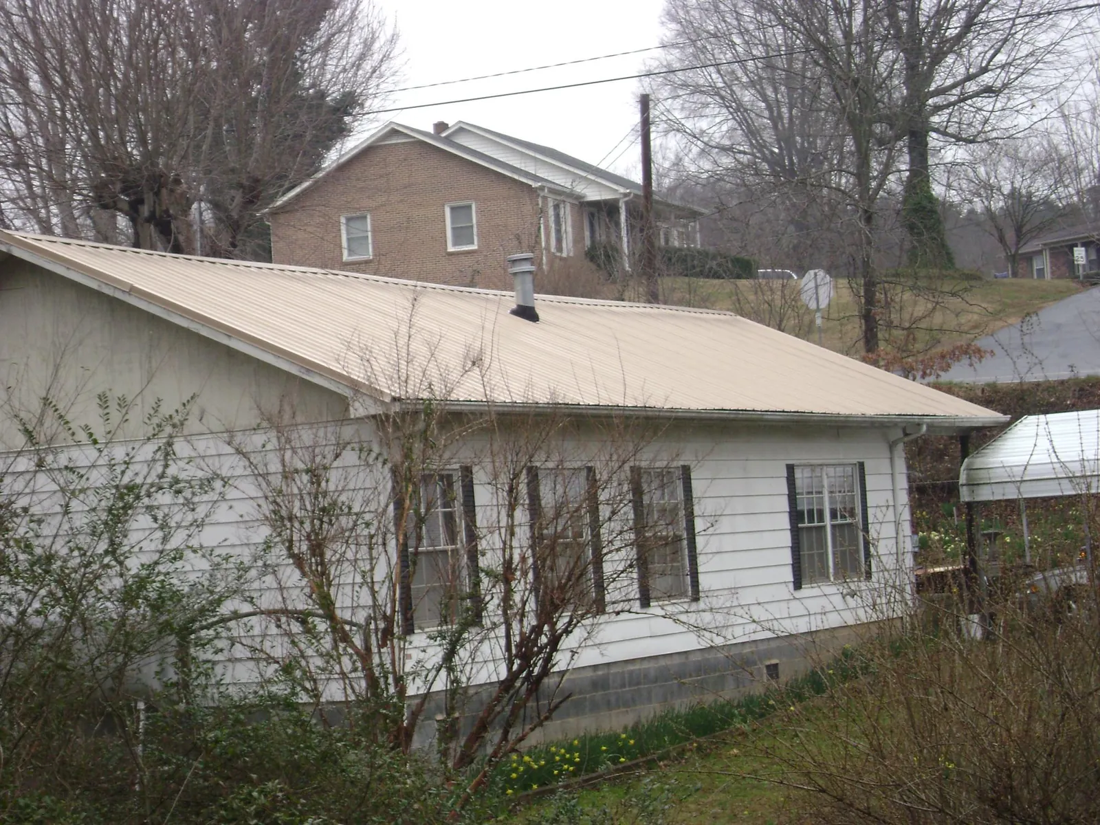 Tan metal roof on a white sided house set into a hillside — Commercial Roofing by Roofing Brothers in Fresno